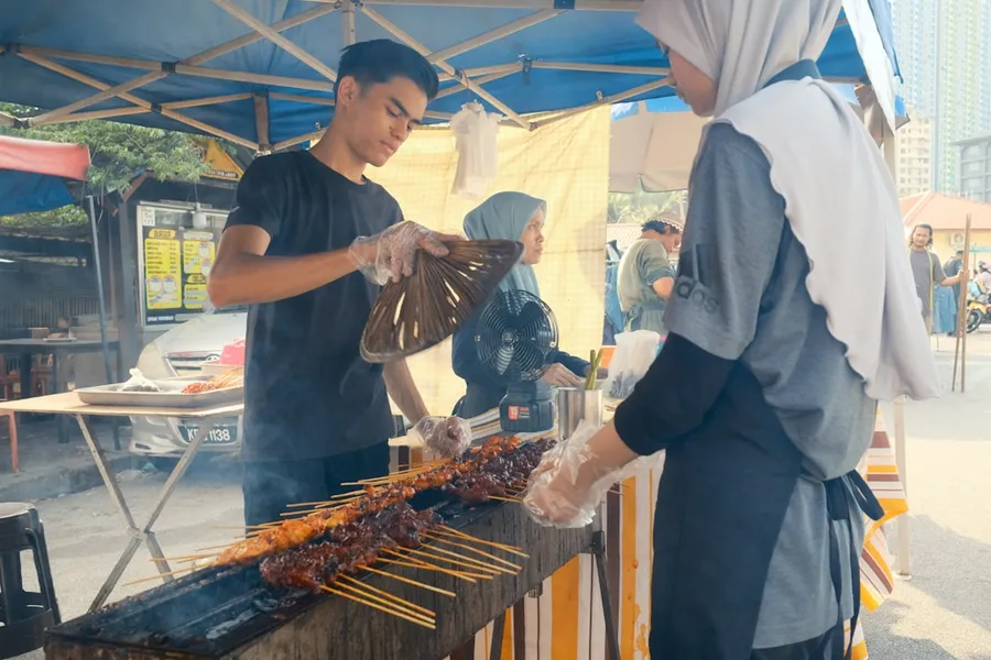 Ilustrasi mimpi tukang sate — People are grilling satay at an outdoor food stall.